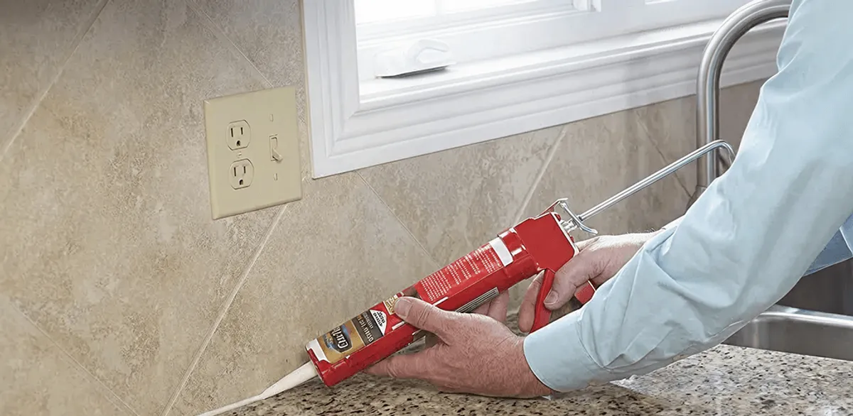 Handyman applying caulk along a kitchen backsplash and countertop seam in Pittsburgh, PA