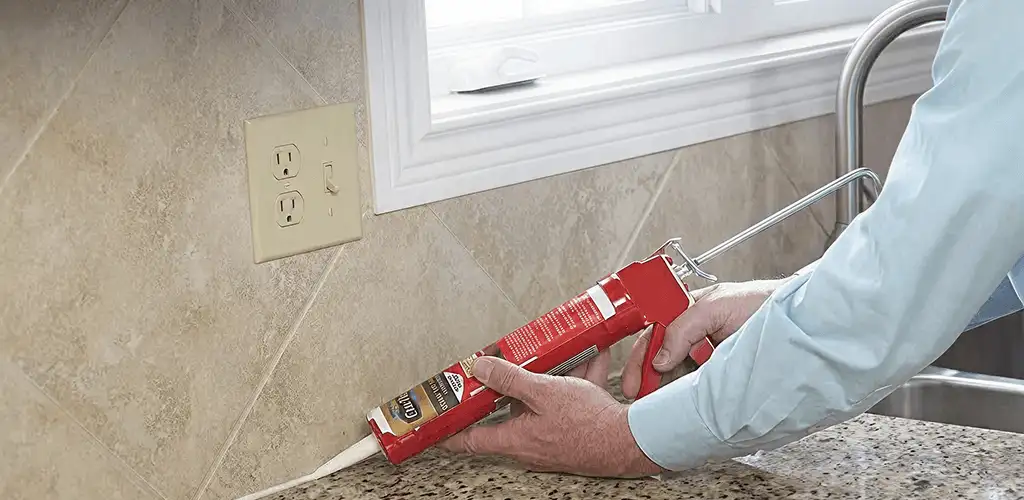 Handyman applying caulk along a kitchen backsplash and countertop seam in Pittsburgh, PA